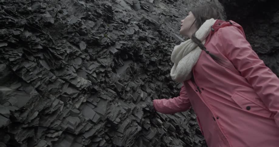 Woman outside brushing her hand against a jagged rock wall