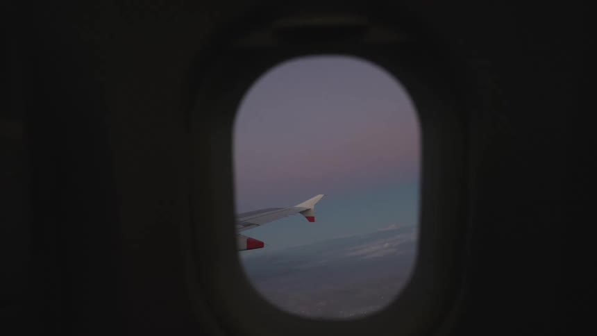 Through the window of an airplane the wings are visible as the plane glides through the sky