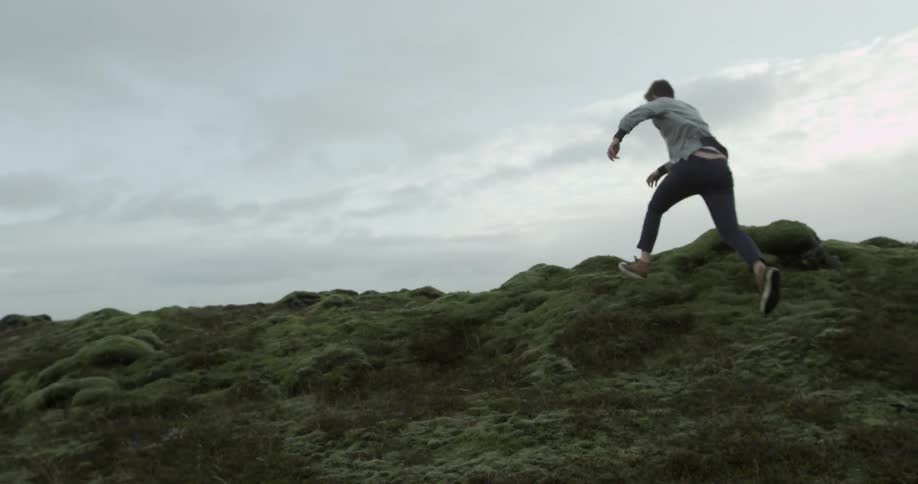 Man jumps over a rocky grassy landscape