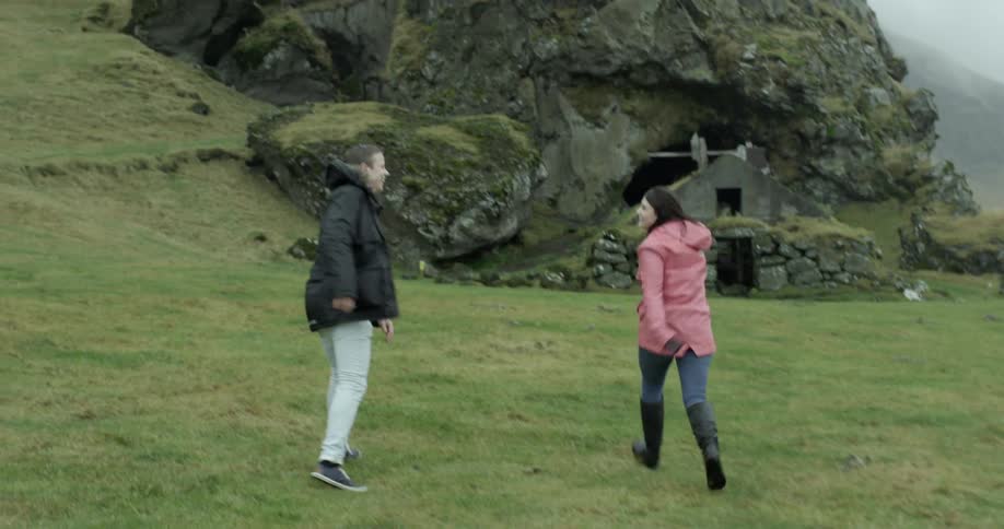 Two women laughing and running in grass at the bottom of a mountain