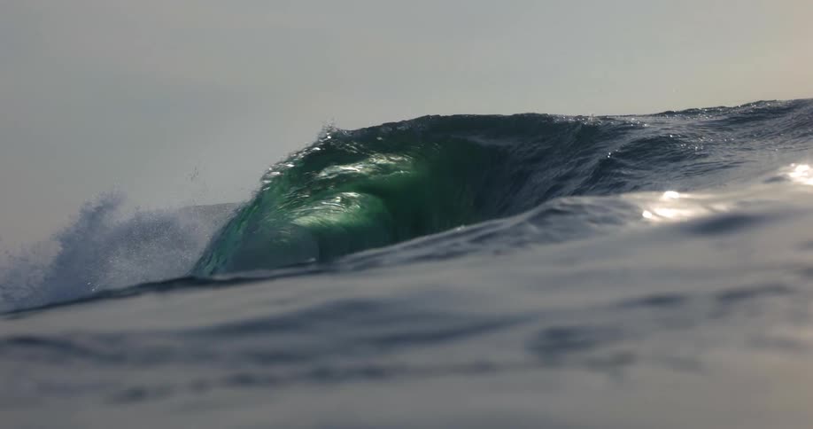 Filmed from the waters surface a powerful ocean wave swells and crests in mesmerizing slow motion its green depths glowing before it breaks