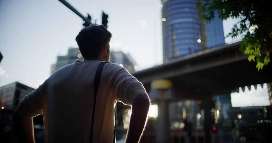 Person standing at an urban intersection looks toward tall buildings and an elevated structure under evening light