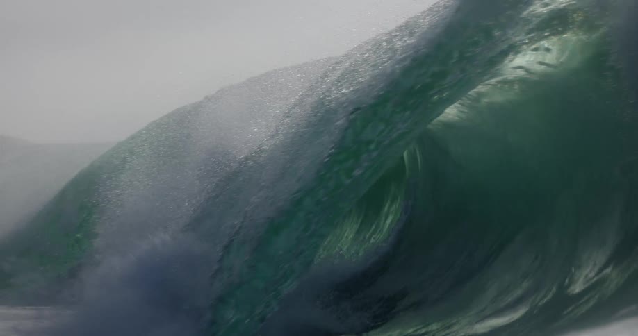 Filmed from inside the water in immersive slow motion a massive ocean wave crests and barrels its green depths revealed before it crashes over the lens