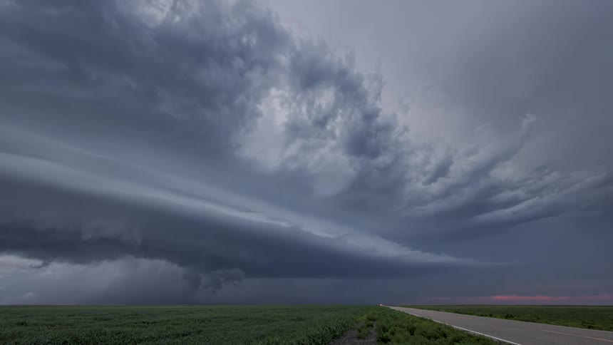 This is a sharp flat horizontal line that separates the dark green field from the dramatic storm clouds above it sits low in the frame emphasizing the vast scale of the sky