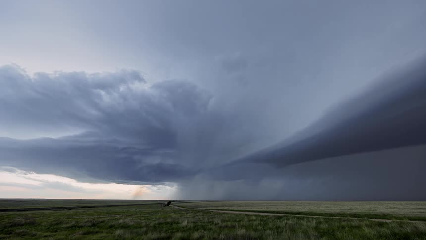Super cell storm moves across the sky pouring rain over rural land as lightning flashes