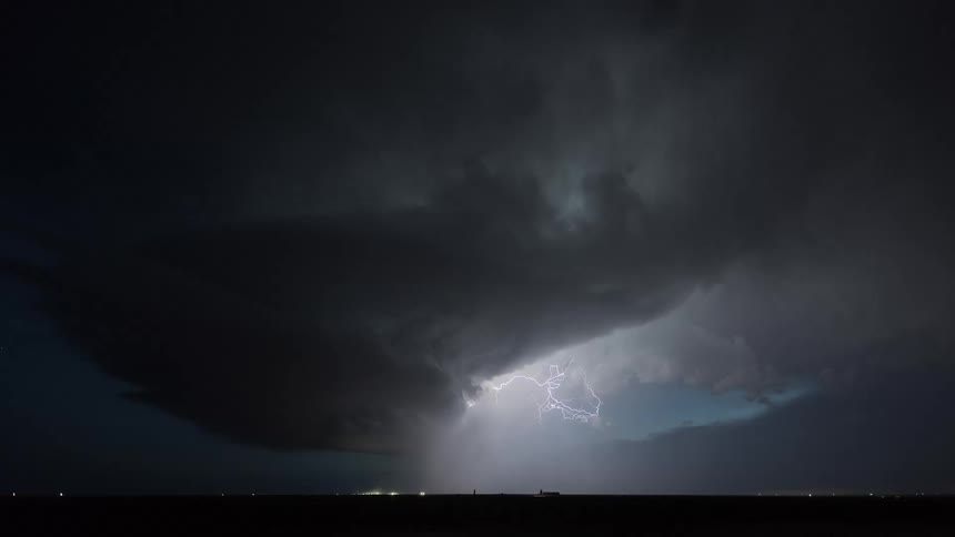 Storm cloud with lightning illuminating a dense formation above the nighttime horizon