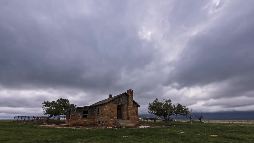 Stone house isolated in an open field with surrounding trees under a cloudy sky and wide horizon