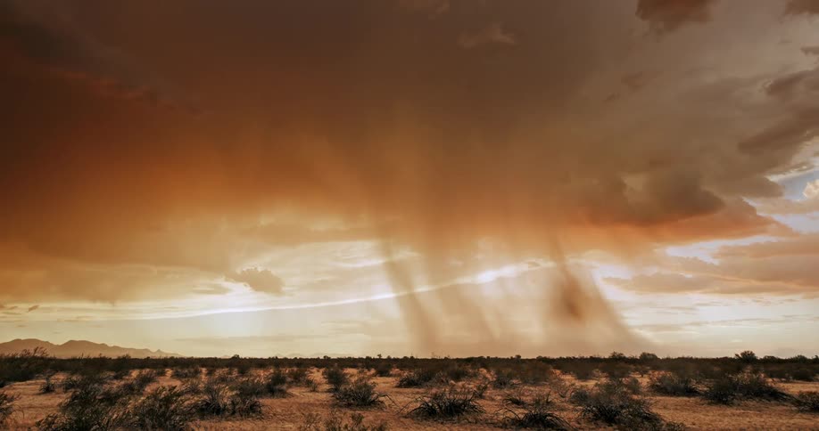 Sunlight breaks through dark orange storm clouds over a vast desert plain