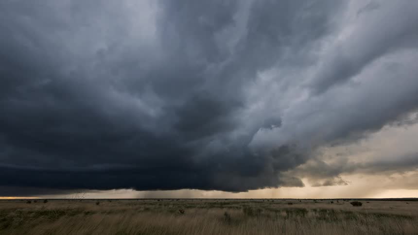 Dark storm clouds loom over a vast grassland plain under a heavy overcast sky