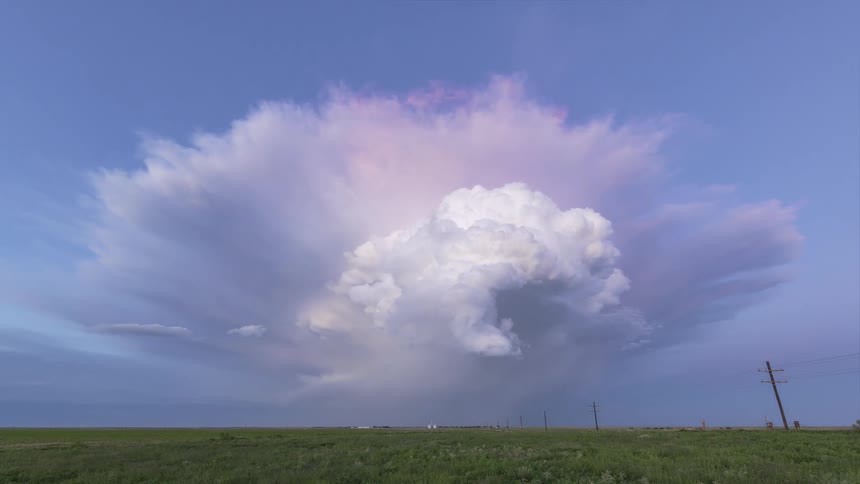 Clouds moving and turning over rural land as traffic moves on the road