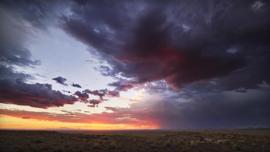 Dramatic storm clouds gather over a vast desert landscape during a vibrant sunset