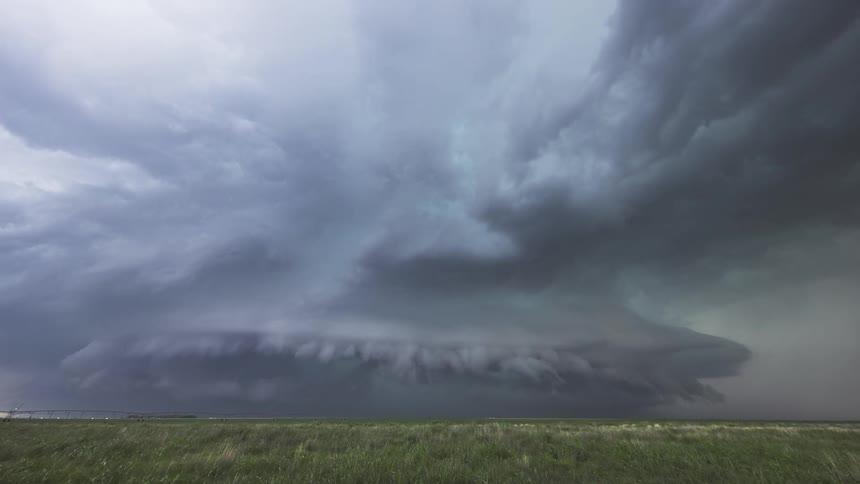 This is a flat steady horizontal line that separates the green grassy field in the foreground from the massive storm clouds filling the sky it remains level throughout the timelapse providing a sense of scale for the approaching weather system