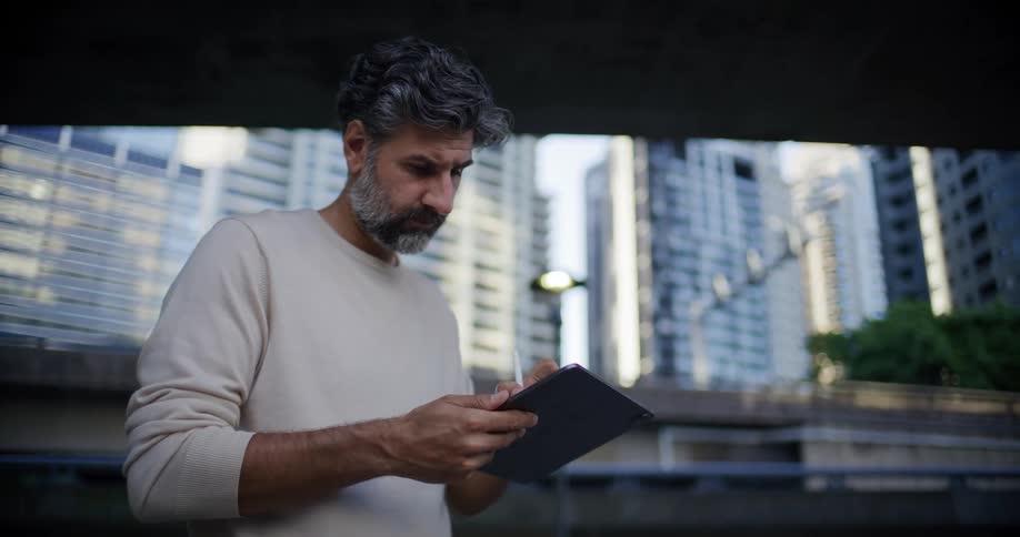 The man is writing on his tablet under the overpass