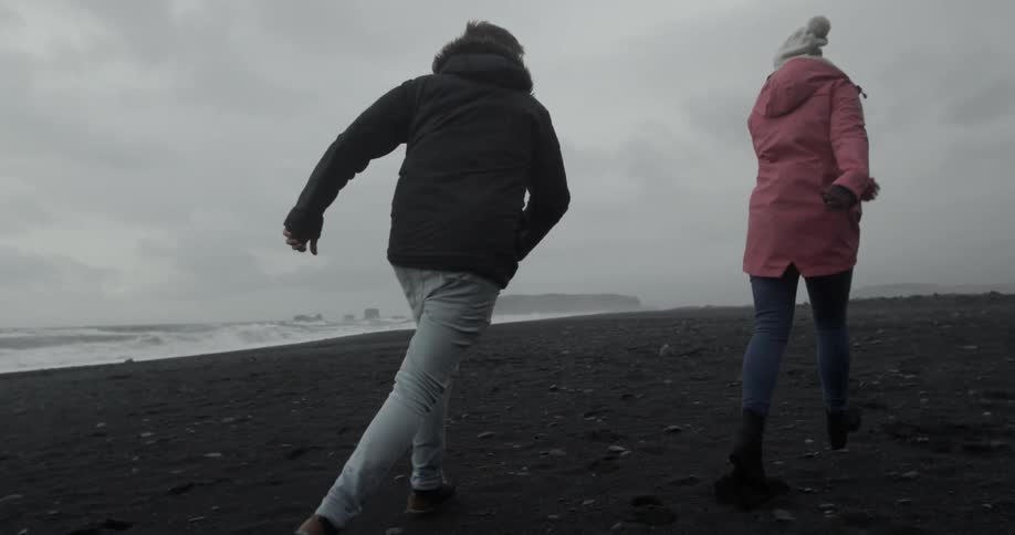 Two people run towards the water holding hands