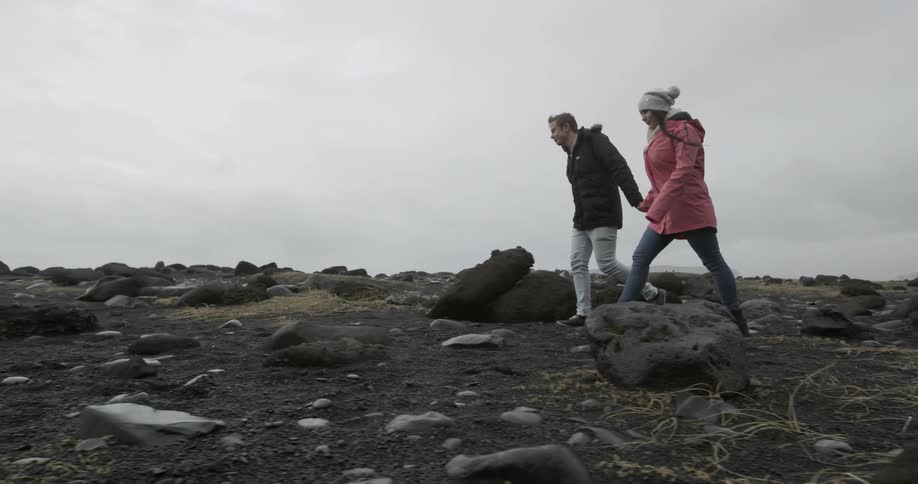 Man and woman holding hands and walking on flat rocky terrain