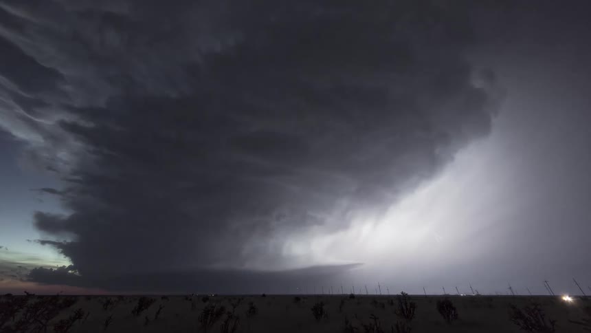 A massive supercell storm cloud looms over a flat plain at dusk