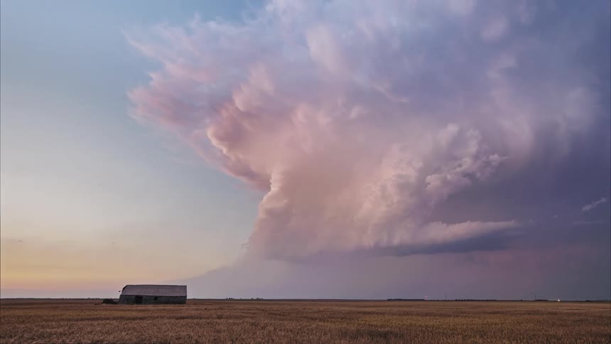 A massive supercell storm cloud looms over a flat plain at sunset