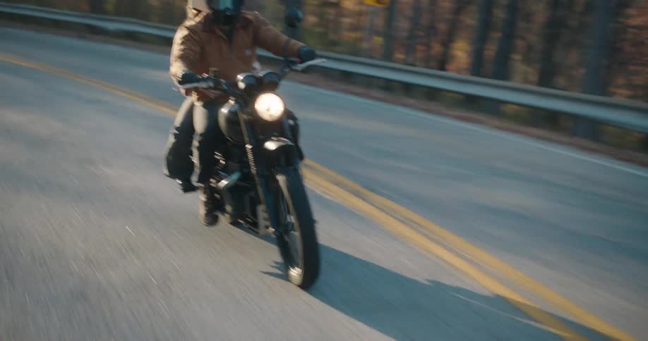 Two people on a motorcycle traveling along a road surrounded by trees