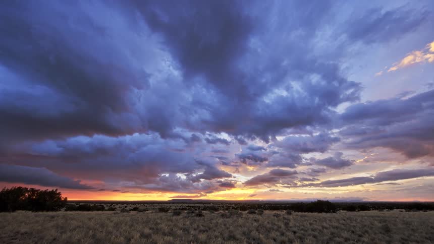 In a stunning timelapse dark storm clouds sweep across a vast prairie catching the brilliant colors of the sunset as day turns into night