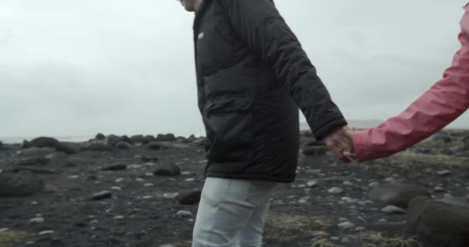 Couple holding hands as they walk through a rocky field on a chilly, cloudy day