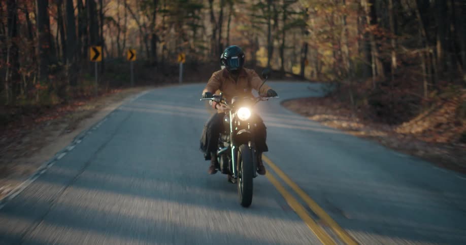 Headlight glows on a motorcycle traveling with a passenger on a road through the forested mountains