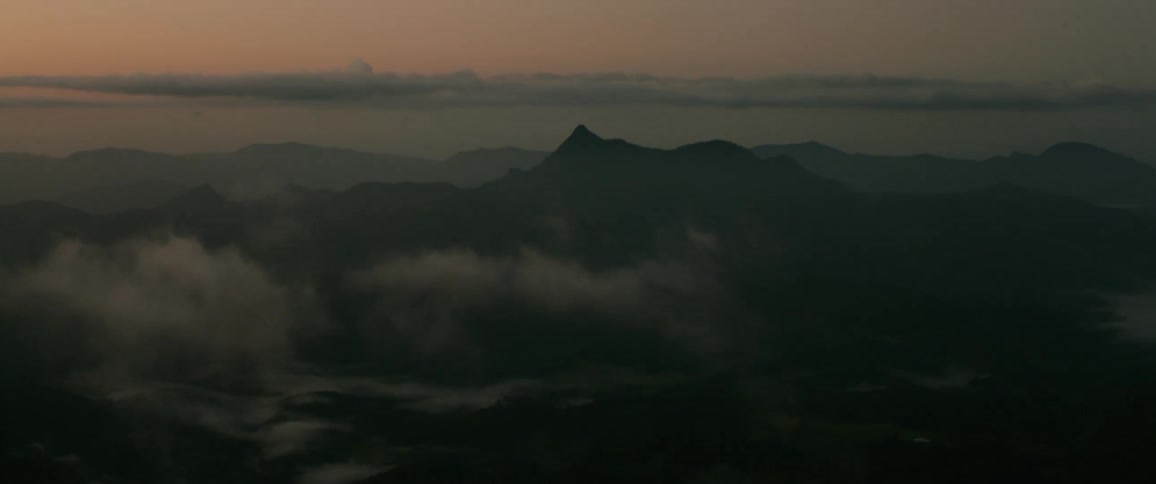 A serene aerial view captures silhouetted mountain peaks rising above a layer of morning fog under a muted predawn sky