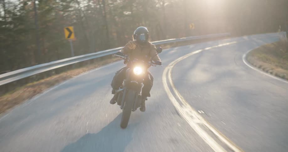 Headlight glows on a motorcycle traveling with a passenger on a road through the forested mountains