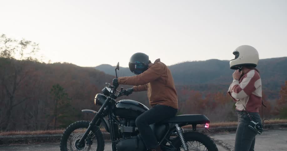 Man and woman alights from a motorcycle with helmets on at dawn