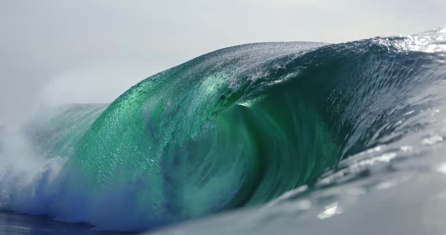 Massive wave forms translucent barrel with white foam under bright sunlight