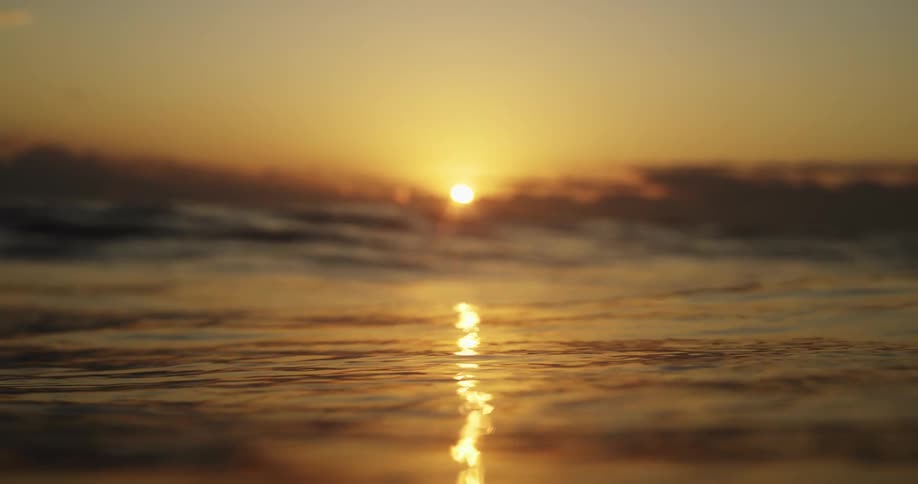 From the waters surface the setting sun casts a warm golden glow its light reflecting across the gently moving ocean waves