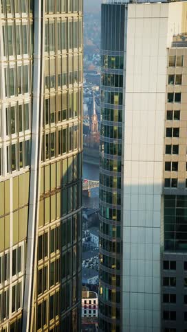 Peeking between the towering glass facades of modern skyscrapers a historic church steeple and a bridge over the river are framed in the distance
