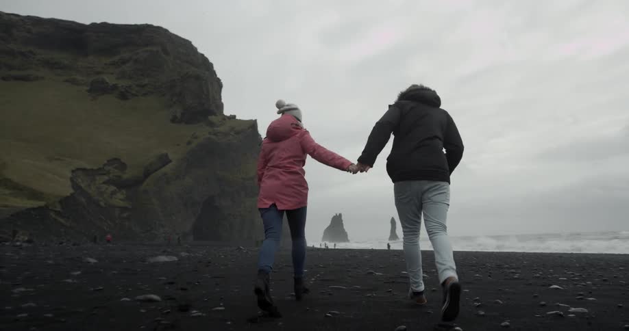 Two people run by the shore holding hands