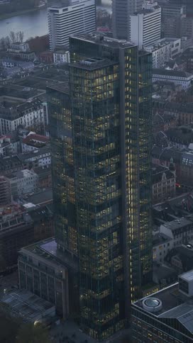 Corporate skyscraper with illuminated offices stands out among surrounding urban buildings at dusk
