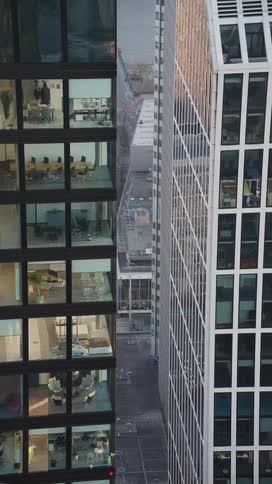 Tall commercial buildings reveal lit office spaces through glass facades with a narrow street running between the structures
