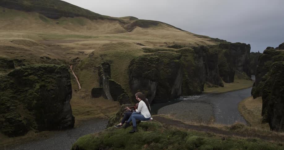 Two people sit on a mountain top overlooking a river