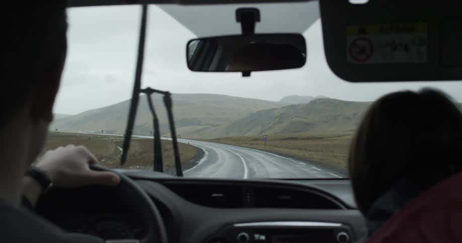 Two people drive down a winding road in the rain