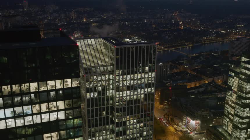 Lit office buildings at night with steam rising from rooftop of glass skyscraper