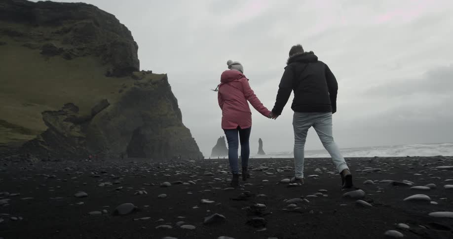 Man and woman hold hands while walking on a cold rocky beach