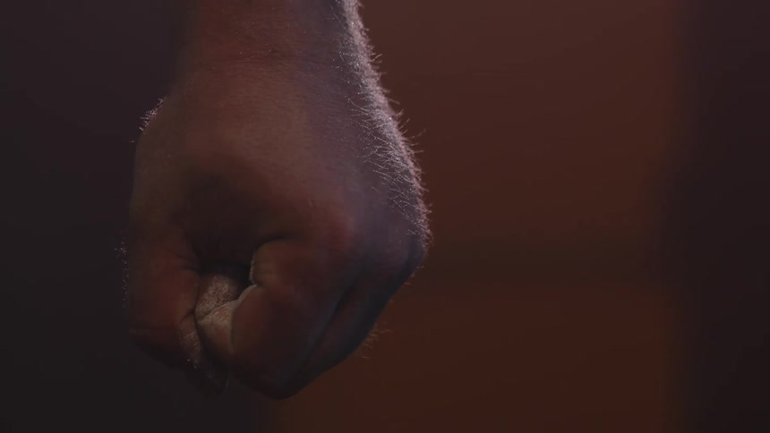 A man standing suddenly balls up his muscular hand into a fist
