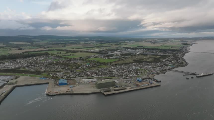 Aerial view of a coastal town with an industrial harbor residential areas and farmland in the background under a cloudy sky