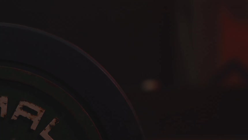 Circular weight plate appears in closeup under low lighting in a workout environment