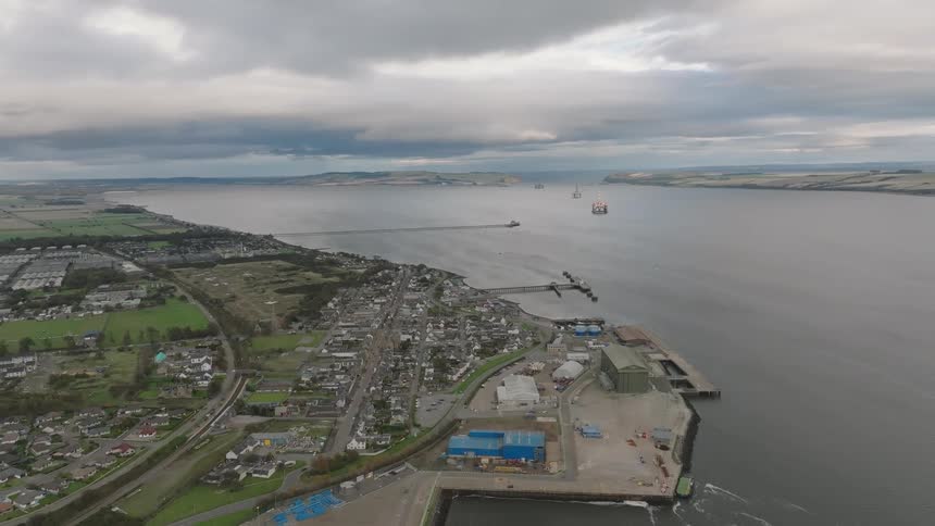 Aerial view of a coastal town with a port residential areas industrial facilities and vessels in the estuary under a cloudy sky