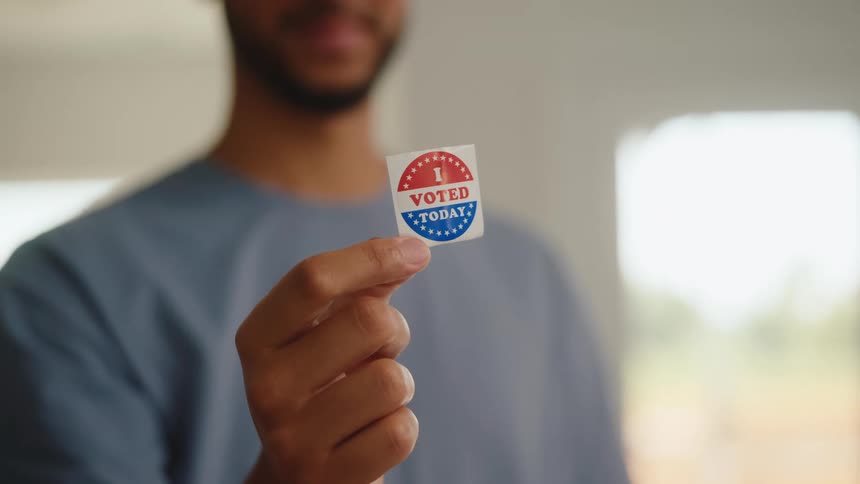 Person holds a sticker reading i voted today in a welllit indoor setting