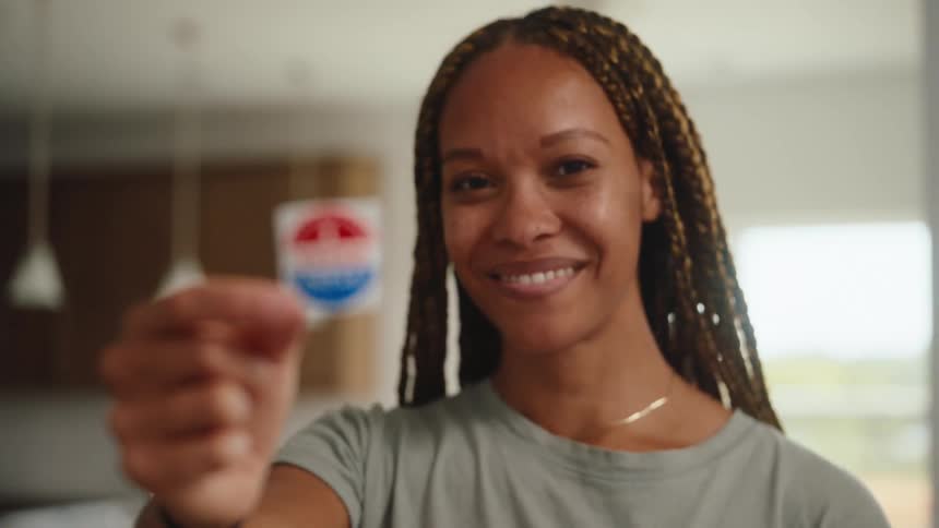 The woman is holding up a sticker that says i voted today