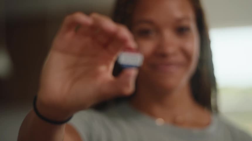 In this video a smiling woman with braided hair looks directly into the camera she slowly brings her hand forward to reveal a small circular sticker that reads i voted