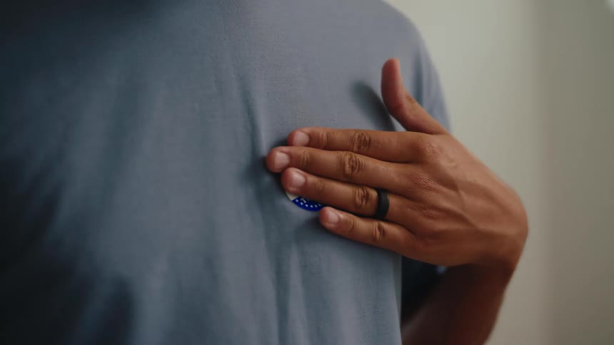 A person in a blue shirt holds an i voted today sticker against their chest the red white and blue design