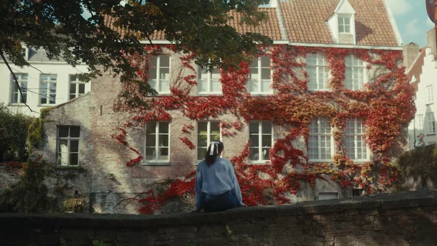A young woman sitting contemplatively on a stone fence outdoors during daytime