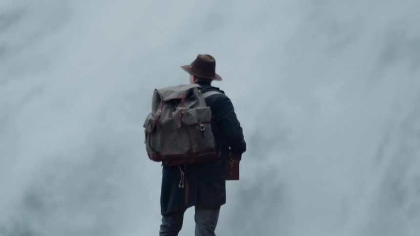 Man wearing a backpack stands watching a nearby waterfall on an autumn day