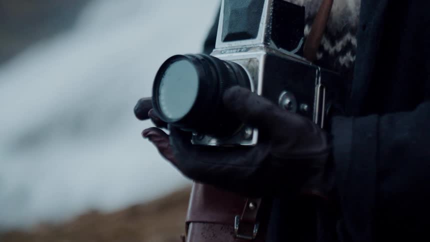 Analog photographic camera is held by gloved hands in an outdoor environment