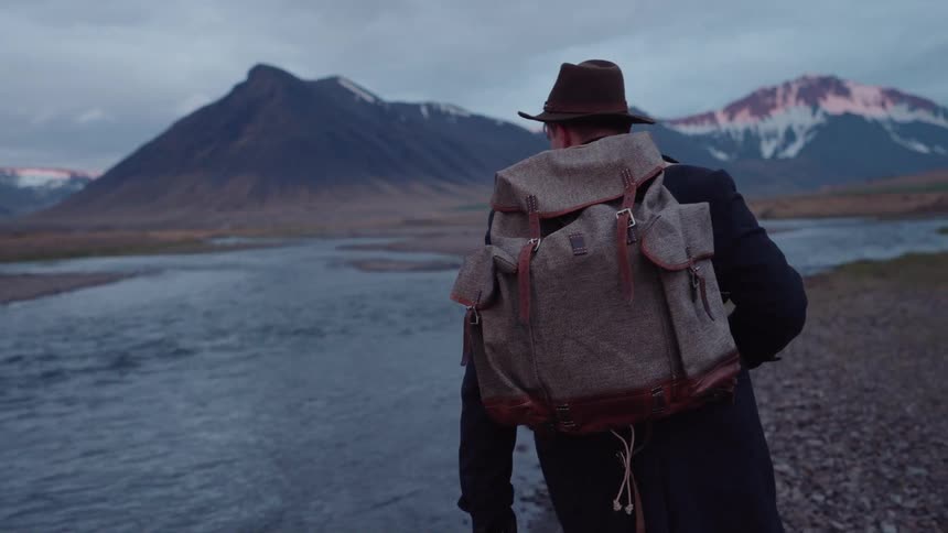 A person walks along a creek in front of a mountain range